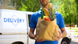 a man holding a bag of groceries by a delivery van
