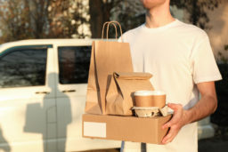 delivery person holds coffee cups and bags of food